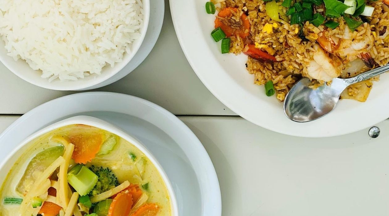 A bowl of rice a bowl of green curry and a bowl of Thai fried rice and vegetables