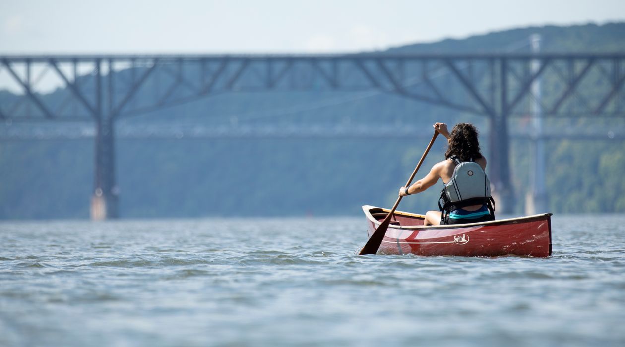 One female in a kayak paddles toward a bridge
