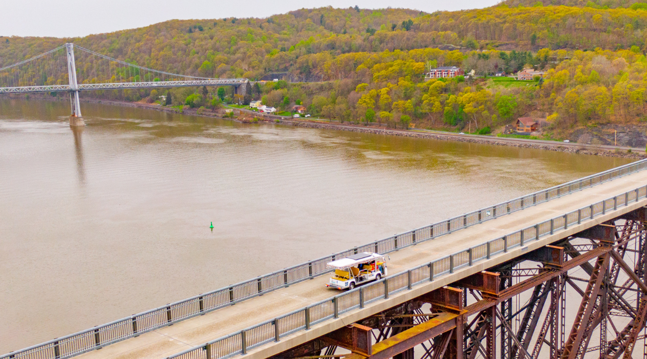 Electric tram crosses the Walkway Over the Hudson, an elevated bridge over a large body of water the Hudson River