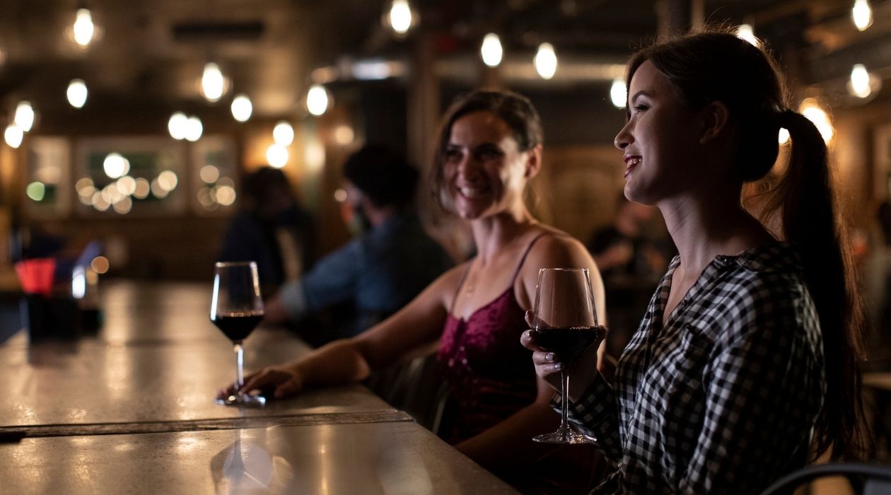 Two women sipping red wine at a bar with string lights in Poughkeepsie